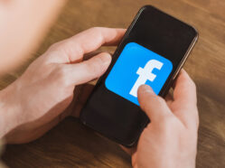 Muž drží mobilní telefon a dívá se na logo facebooku.
